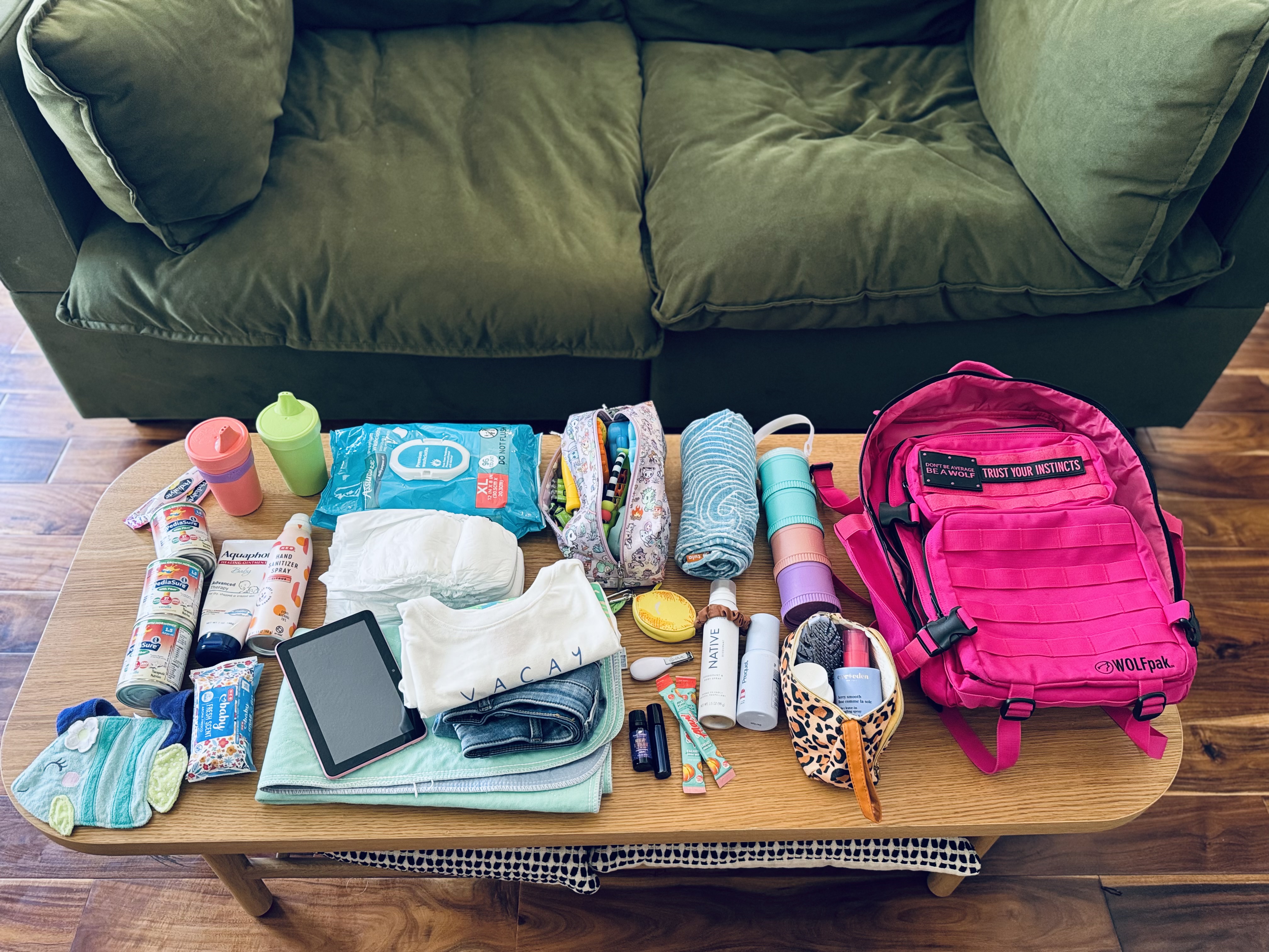 Flat lay of hospital bag essentials including pediasure, bottles, wipes, diapers, tablet, clothes, medical supplies and a Wolfpack brand backpack