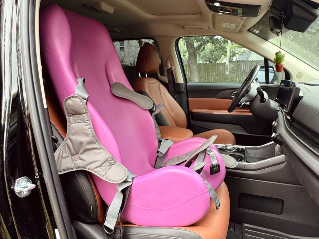 Special Tomato Soft-Touch Sitter in front seat of parked car — adaptive seating for long waits during sibling activities