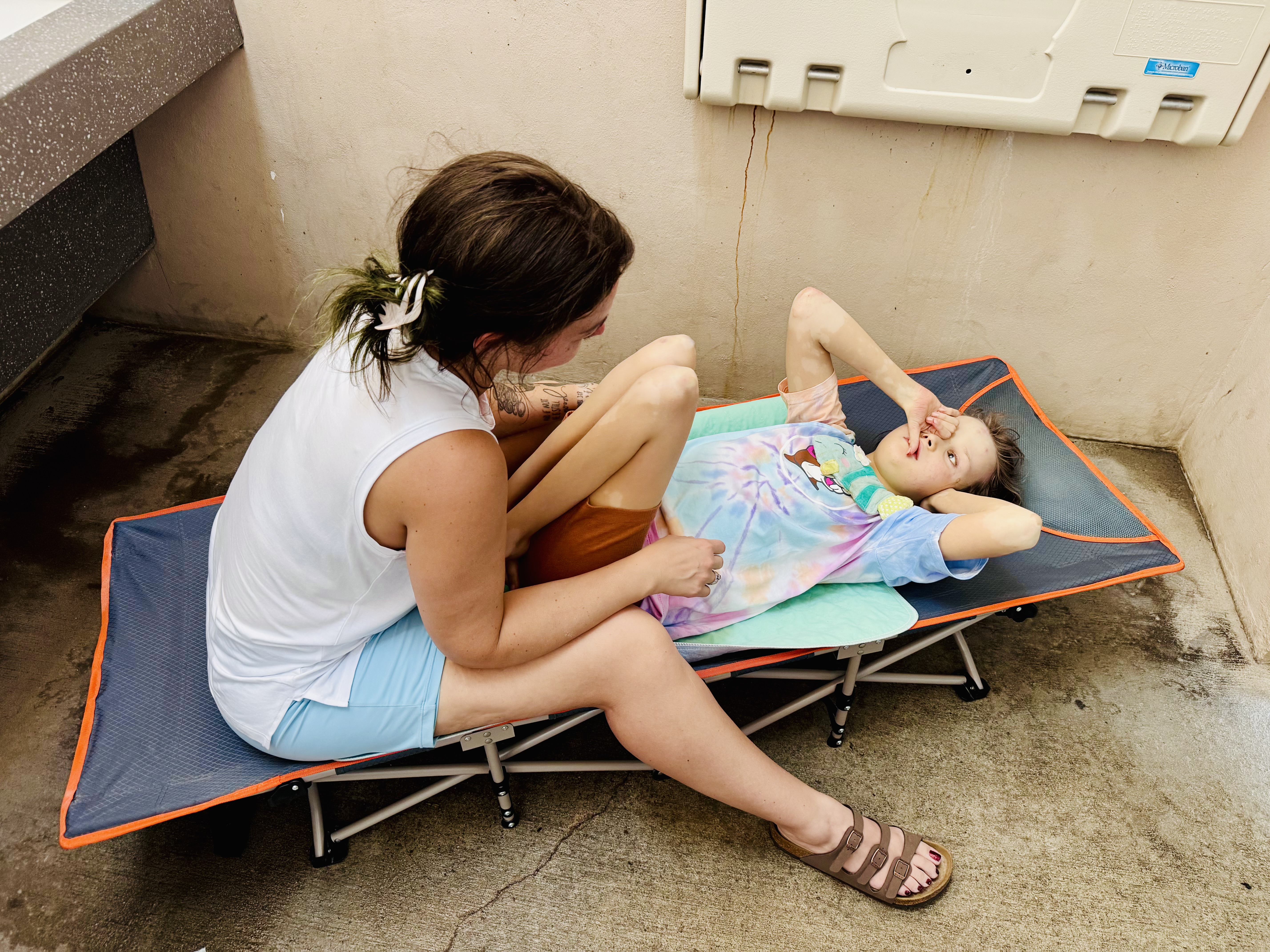 medically complex child lying on camping cot in family restroom at Mustang Island below infant changing table on wall
