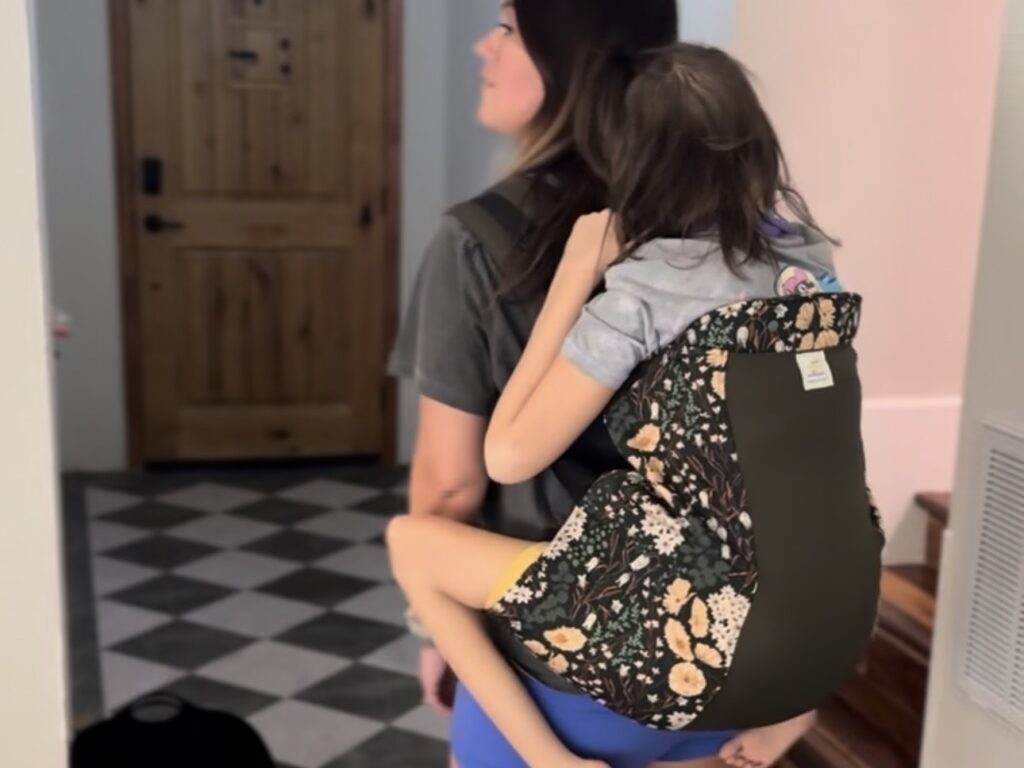 Mother carrying teen showing Kinderpack floral baby carriers for bigger kids