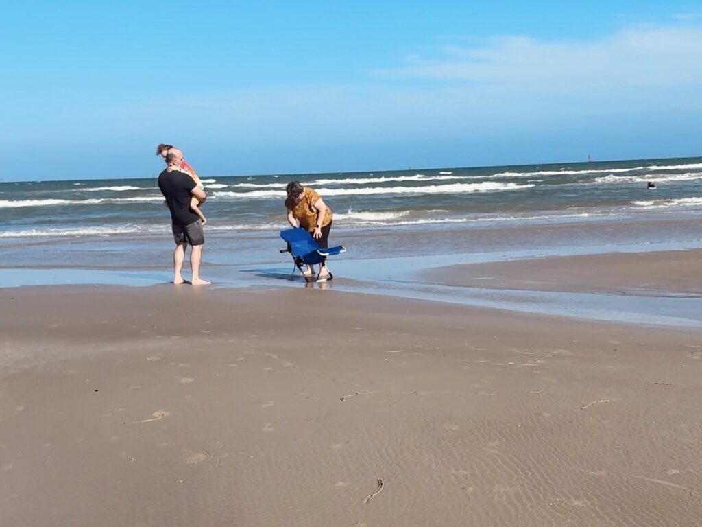 two adults setting up adaptive bath chair at water's edge for medically complex child